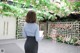 A woman standing in front of a flower covered wall.