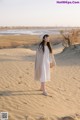 A woman in a white dress standing in the sand.