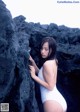 A woman in a white bathing suit leaning against a rock.